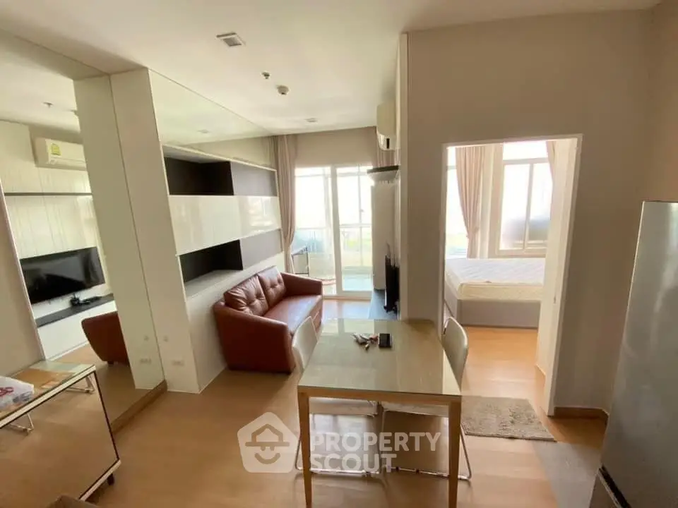 Modern apartment interior with open living room and bedroom, featuring sleek furniture and natural light.