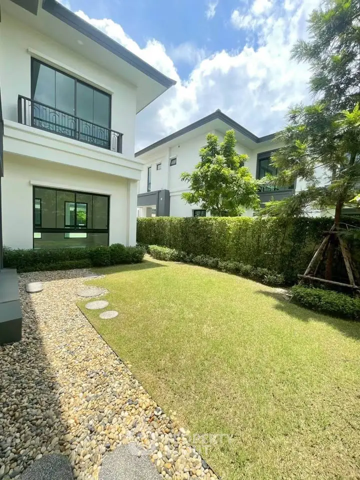 Modern two-story house with lush garden and stone pathway under a bright blue sky.