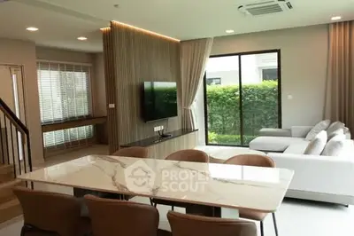 Modern open-plan living room with elegant marble dining table and cozy seating area, featuring large windows and lush garden view.