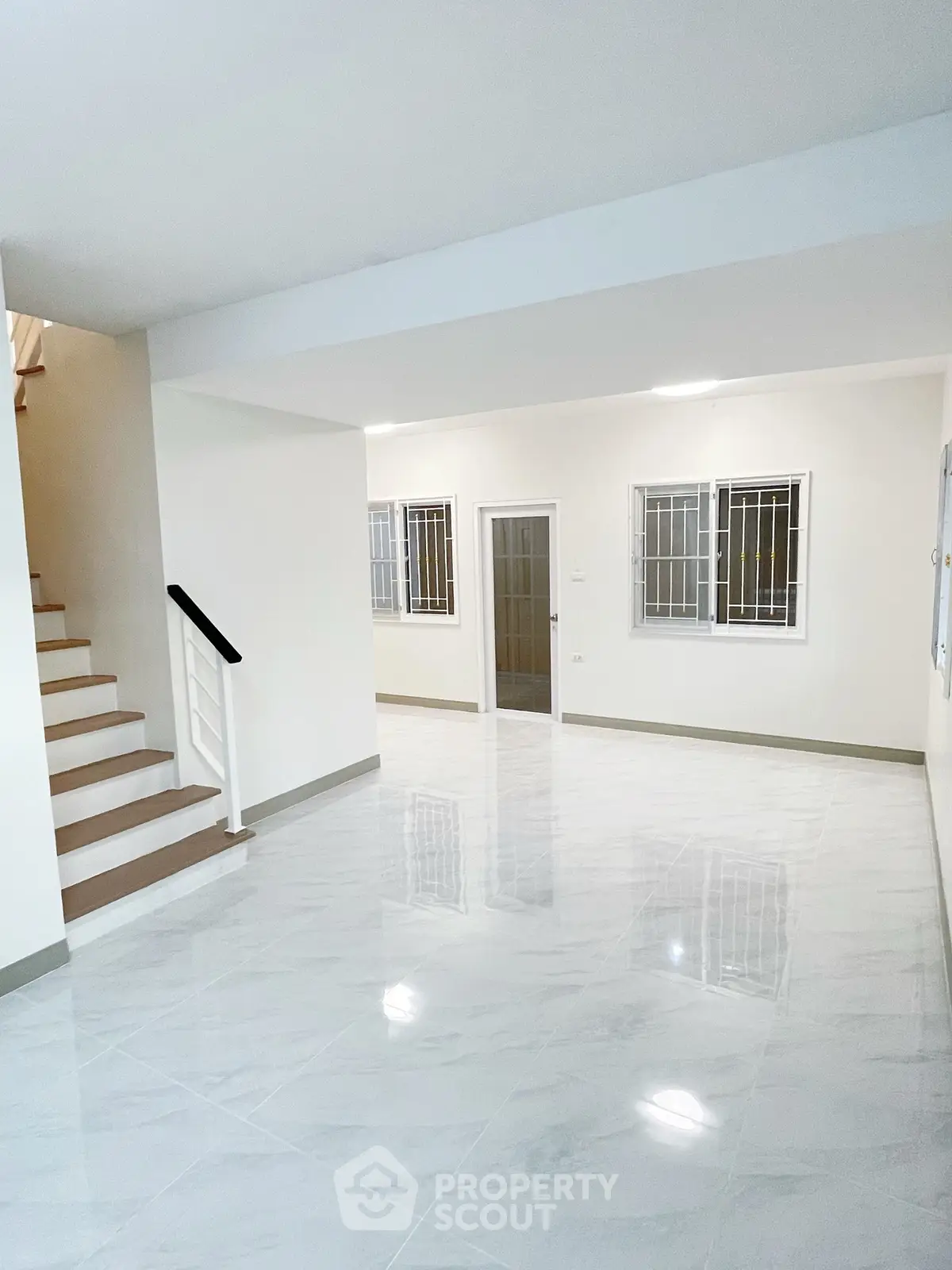Spacious modern living room with glossy tiled floors and staircase, perfect for family gatherings.