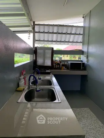 Modern outdoor kitchen with dual sinks and microwave under a covered patio.