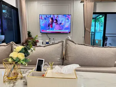 Modern living room with elegant decor and large TV, featuring stylish furniture and natural light.