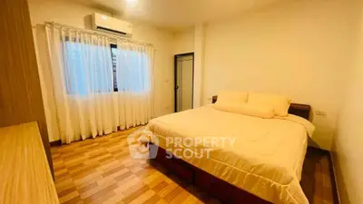 Cozy bedroom with wooden flooring and natural light, featuring a comfortable bed and air conditioning.