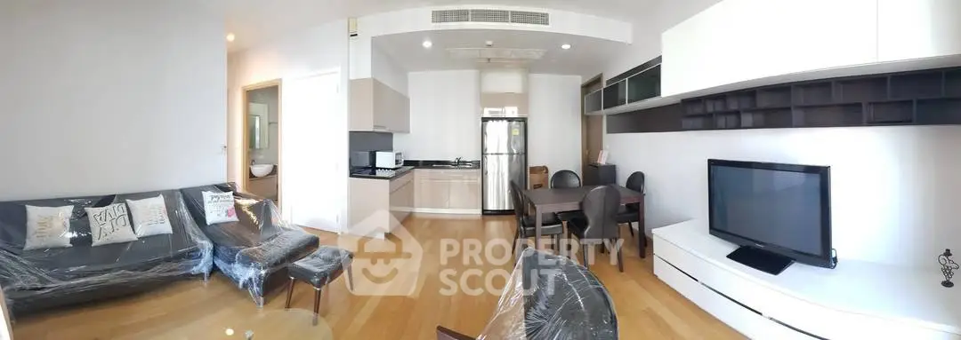 Spacious modern living room with open kitchen, featuring sleek furniture and wooden flooring.