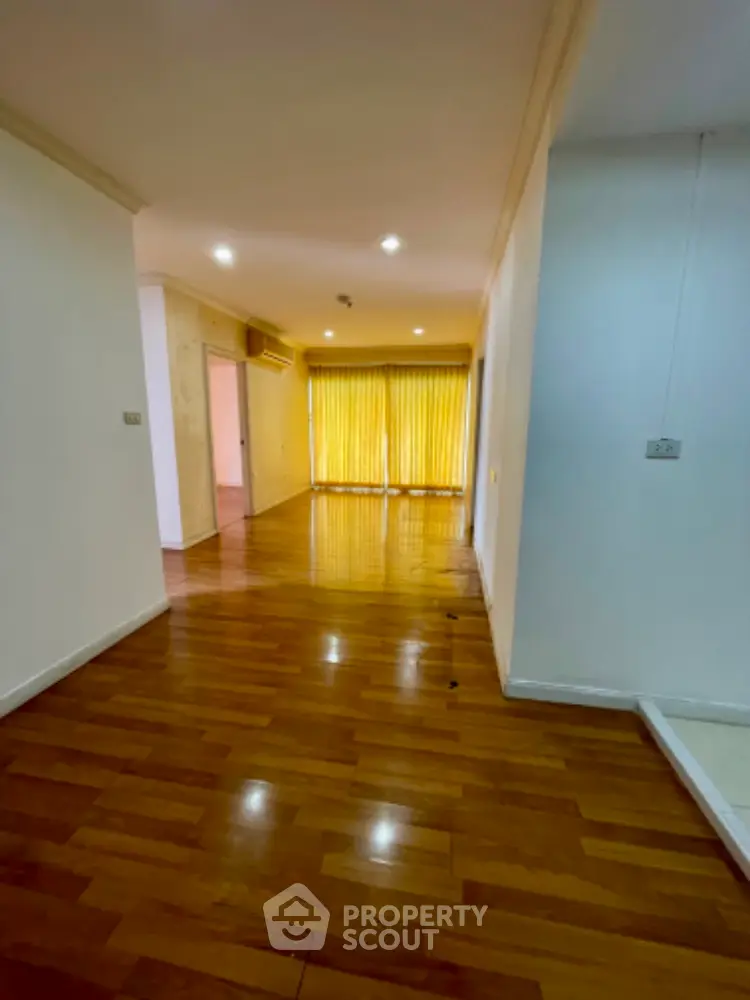 Spacious hardwood floor hallway leading to bright room with large windows