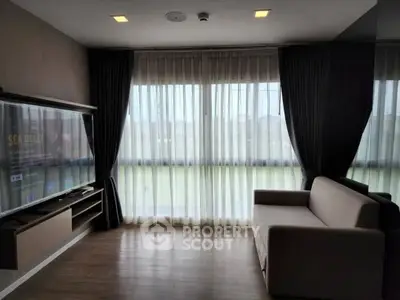 Modern living room with large TV and cozy sofa, featuring floor-to-ceiling windows and elegant curtains.