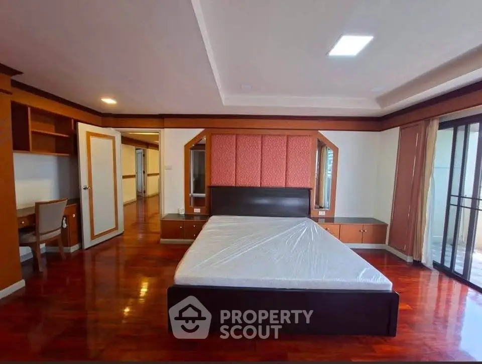 Spacious bedroom with elegant wooden flooring and large windows for natural light.