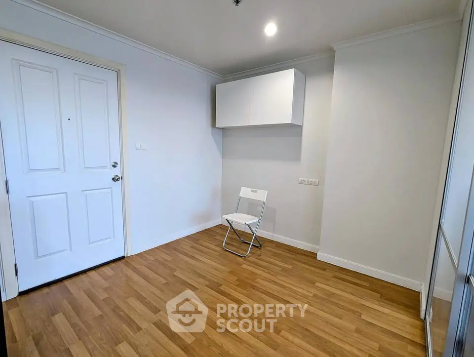 Minimalist room with wooden flooring and white walls, featuring a folding chair and wall cabinet.