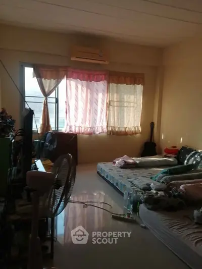 Cozy bedroom with natural light, featuring a mattress on the floor and a window with curtains.