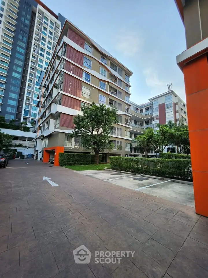 Modern apartment complex with lush greenery and spacious parking area.