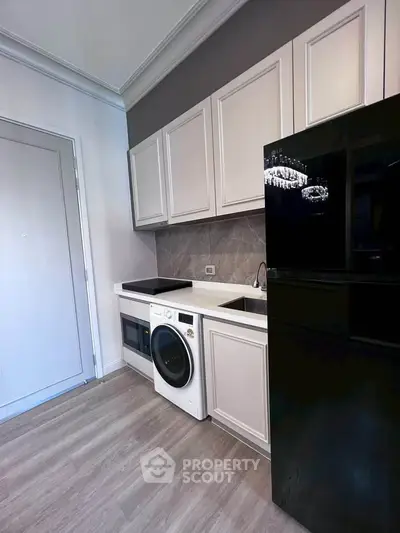 Modern kitchen with sleek appliances and elegant cabinetry, featuring a washing machine and black refrigerator.