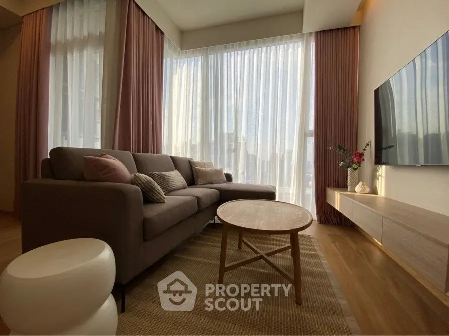 Modern living room with stylish sofa, large windows, and wall-mounted TV in a cozy apartment.