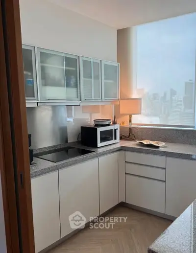 Modern kitchen with sleek cabinets and city view, featuring a microwave and elegant lighting.
