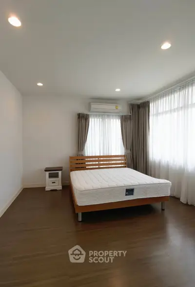 Spacious bedroom with natural light, wooden flooring, and modern decor.