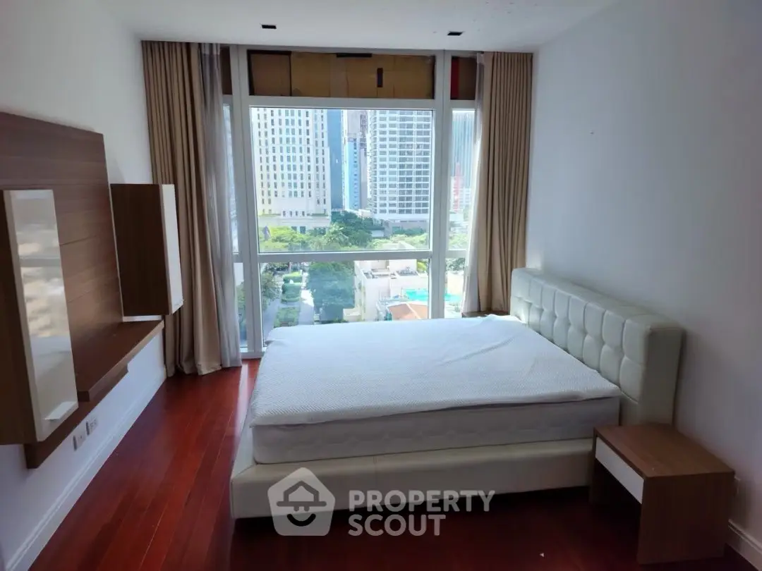 Spacious bedroom with large window offering city view and elegant wooden flooring.
