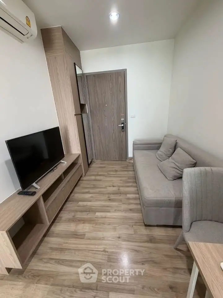 Modern living room with sleek wooden flooring and cozy sofa, featuring a flat-screen TV and stylish decor.