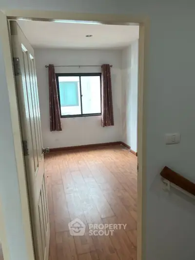 Spacious empty room with wooden flooring and window, ideal for customization.