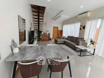Modern open-plan living room with stylish furniture and staircase, featuring a sleek dining area and ample natural light.