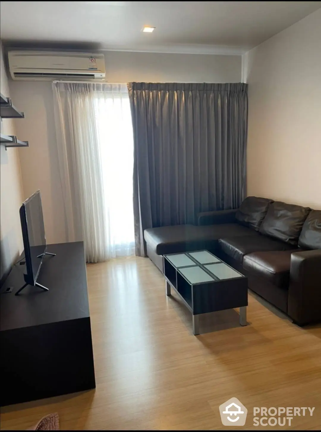 Cozy living room with sleek hardwood floors, comfortable leather sofa, and modern entertainment unit, bathed in natural light from the large window draped with elegant curtains.