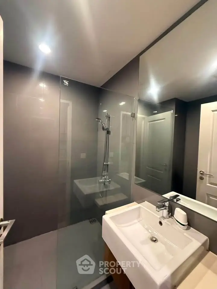 Modern bathroom with glass shower and sleek sink in contemporary apartment.
