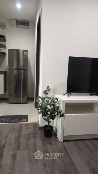 Modern living room with sleek TV stand and stainless steel fridge in open layout.