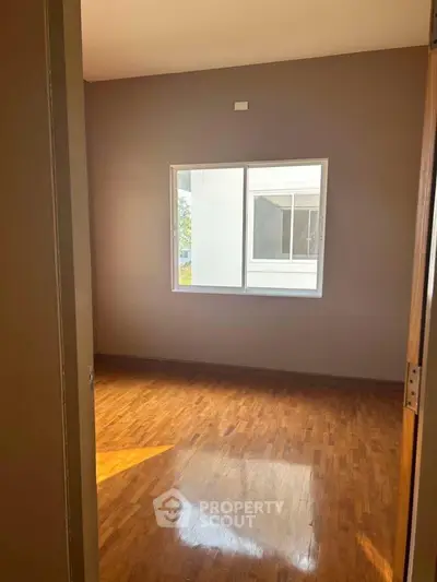 Spacious empty room with wooden flooring and large window offering natural light.