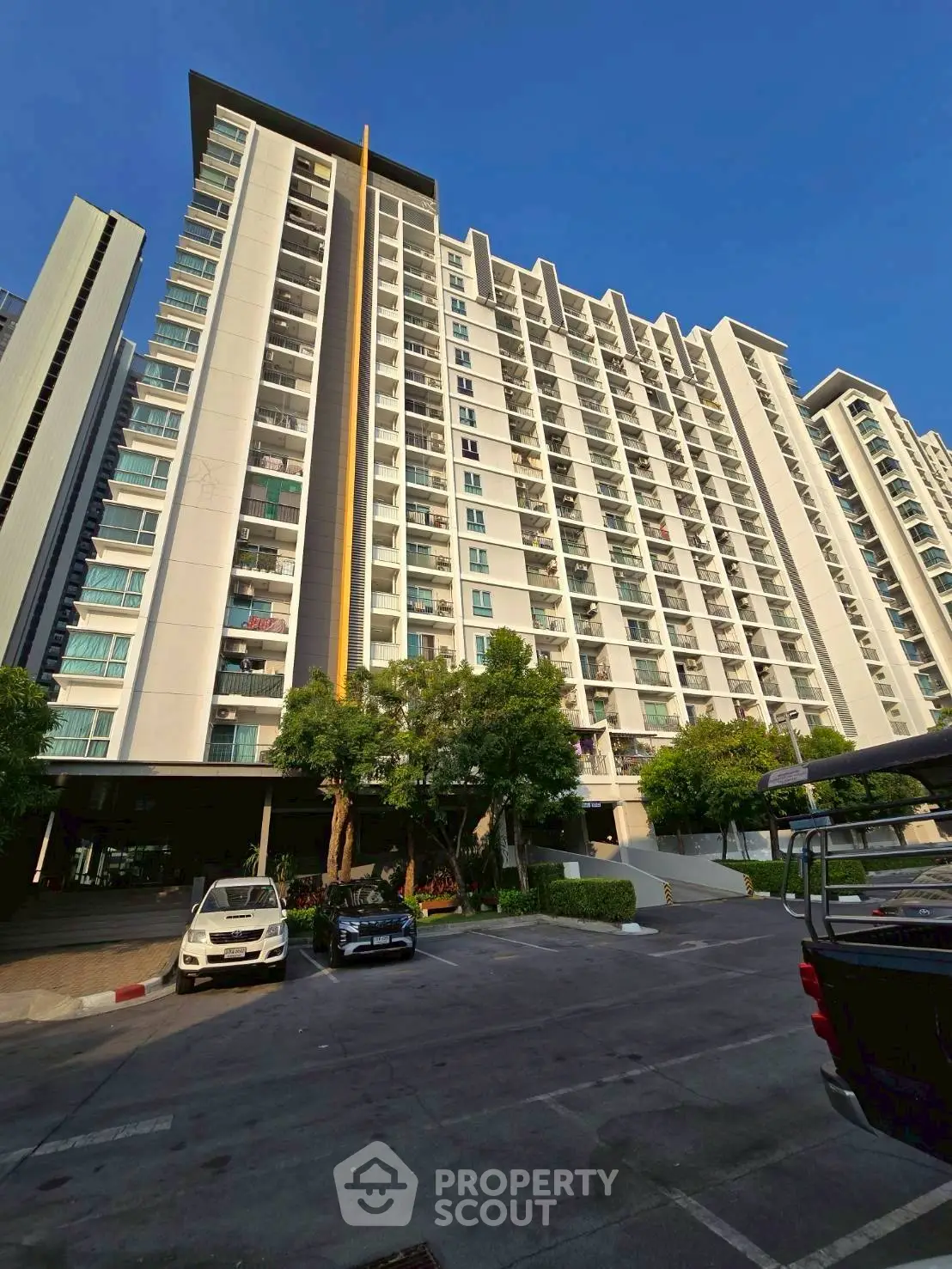 Modern high-rise condominium with spacious balconies and lush greenery in urban setting.