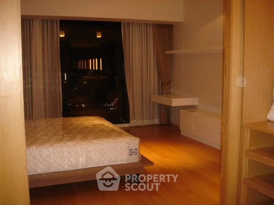 Spacious bedroom with large window offering stunning night views, featuring modern wooden flooring and minimalist design.