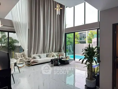 Luxurious living room with high ceilings and pool view, featuring elegant decor and floor-to-ceiling windows.