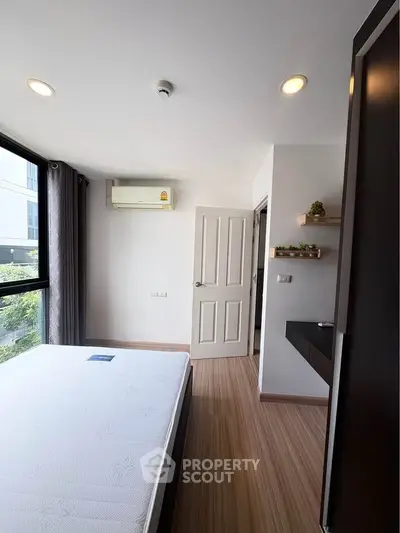 Modern bedroom with large window and wooden flooring in a stylish apartment.
