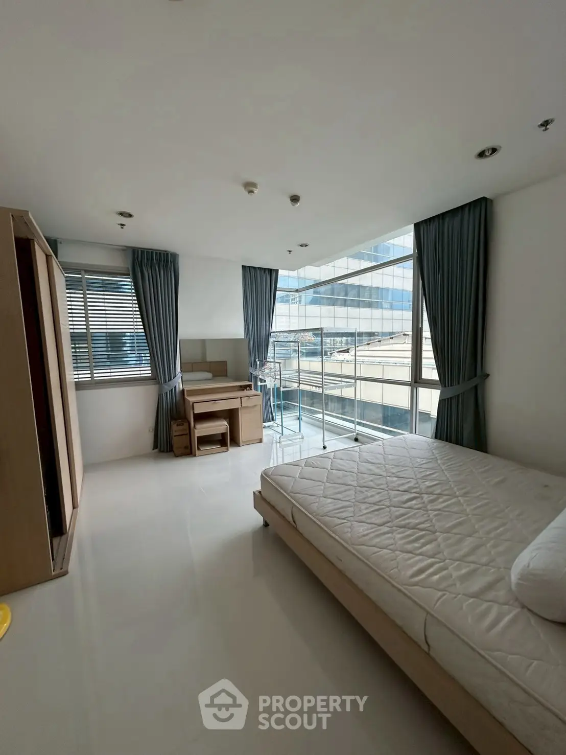 Spacious bedroom with modern furnishings and large windows offering city views.