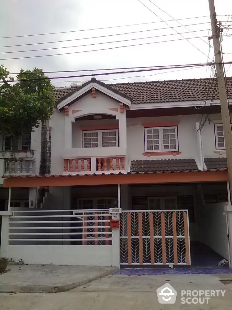 Charming two-story residential home with a classic tiled roof and a secure gated entrance, featuring a spacious carport and quaint upper-level balcony.