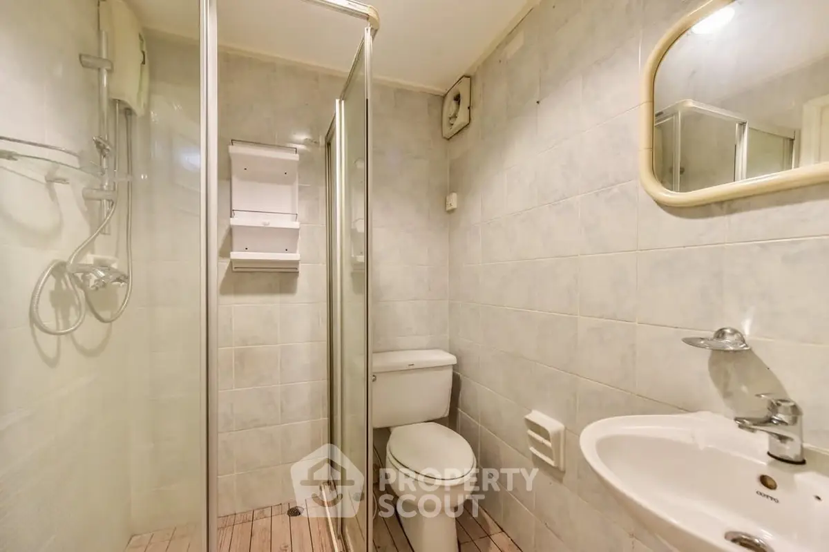 Compact bathroom with shower, toilet, and sink in a tiled setting