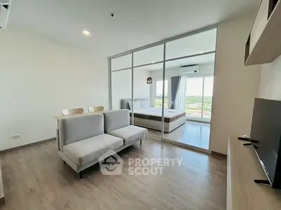 Modern living room with glass partition and view of bedroom, featuring sleek furniture and natural light.