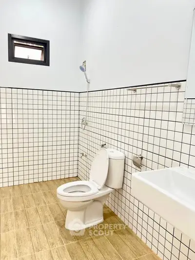 Modern bathroom with tiled walls and wooden floor, featuring a toilet and sink.