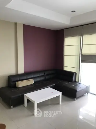 Modern living room with sleek black sectional sofa and white coffee table, featuring stylish purple accent wall.