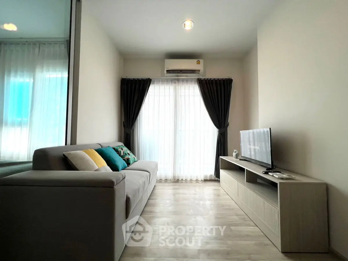 Modern living room with sleek sofa, flat-screen TV, and large window for natural light.