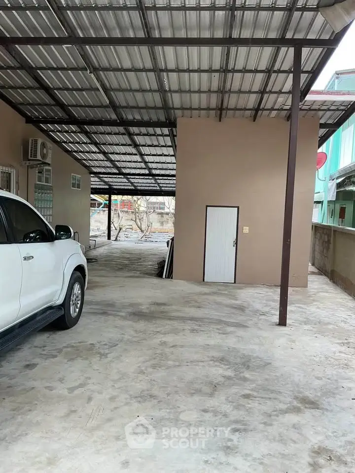 Spacious covered parking area with metal roof and adjacent storage room.