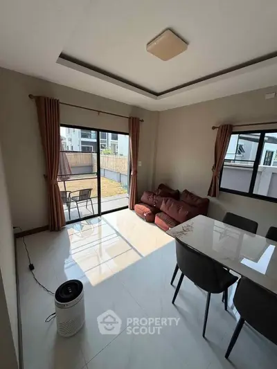 Bright living room with modern dining area and large windows opening to a patio.