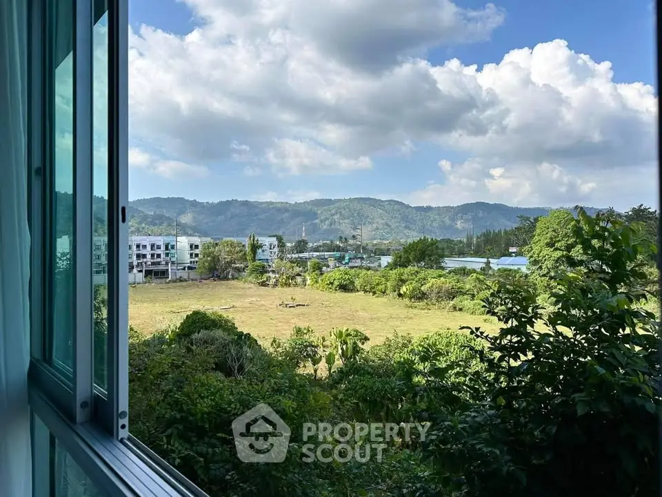 Stunning open window view of lush greenery and distant mountains under a bright blue sky.