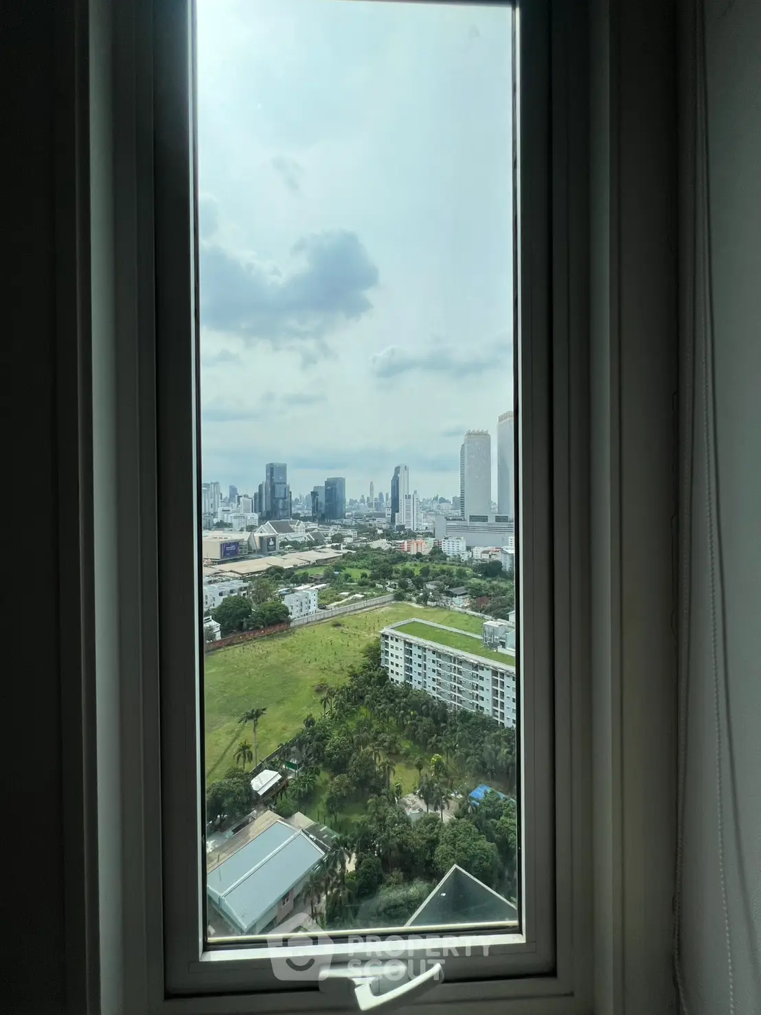 Stunning cityscape view from a high-rise window, showcasing urban skyline and greenery.