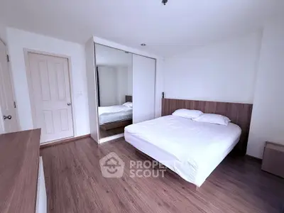 Spacious bedroom with wooden flooring and mirrored wardrobe in modern apartment.