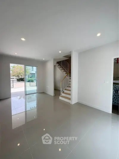 Spacious modern living room with sleek tile flooring and staircase, featuring large windows for natural light.