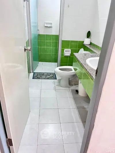 Modern bathroom with green and white tiles, featuring a shower and sleek vanity.