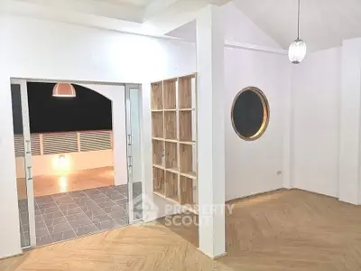 Modern living room with unique circular window and open layout leading to a spacious balcony.