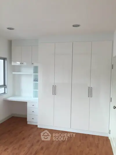 Spacious bedroom with built-in white wardrobe and study desk, featuring elegant wooden flooring.