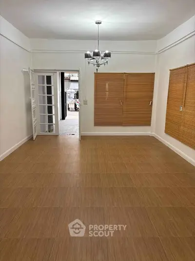 Spacious empty room with wooden blinds and chandelier, ideal for customization.