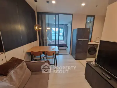 Modern open-plan living room with kitchen and bedroom view, featuring sleek furniture and appliances.
