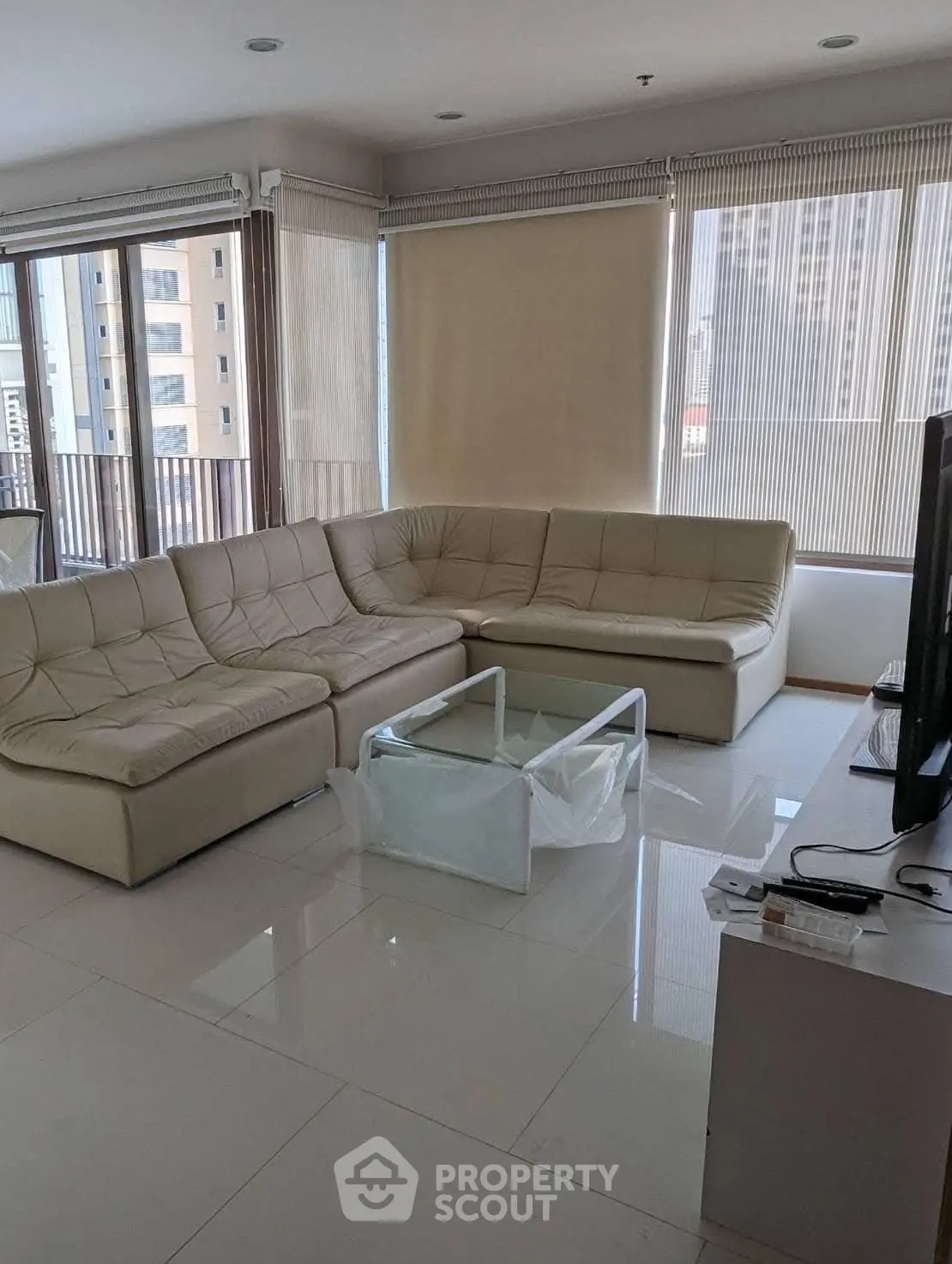 Spacious living room with modern beige sectional sofa and large windows offering city views.