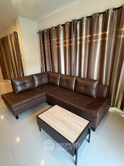 Modern living room with sleek brown leather sectional sofa and elegant curtains.